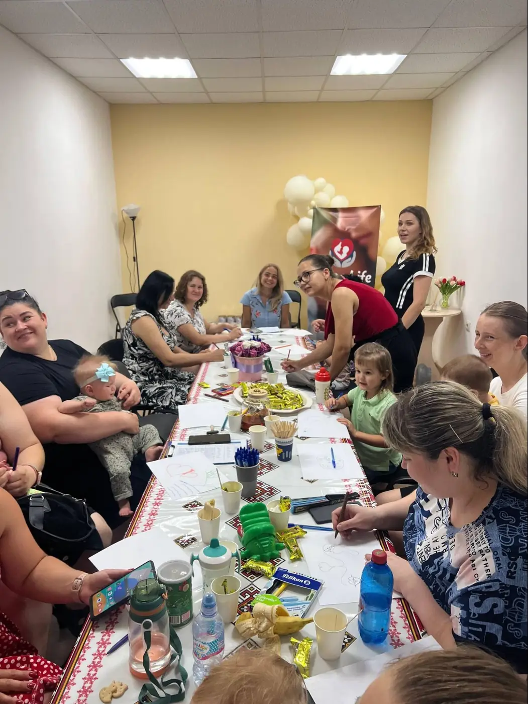 Mothers and their young children sit around a long table during a parenting class at Life Center Zhytomyr.